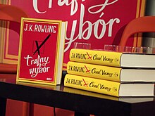 Une pile de trois livres au dos jaune est posée sur une table avec un exemplaire posé de face. La couverture de celui-ci est rouge encadrée de jaune. L'illustration est une simple case cochée d'une croix et le nom de l'auteure et le titre du livre sont écrits en blanc de part et d'autre de l'illustration.