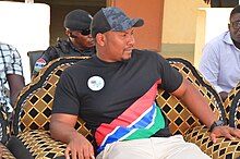 Talib Ahmed Bensouda wearing a shirt with the Gambia flag and a badge with the Kanifing coat of arms.