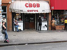 Entrée d'un bâtiment avec un store blanc portant l'inscription CBGB en rouge dessus.