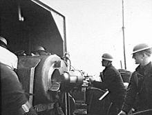 Gunners wearing steel helmets load a shell into a large calibre weapon