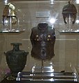 Hoplite armour exhibit. Note the gold inserts around the chest area of the bronze upper torso plate at the centre of the exhibit. The helmet on the upper left is a restored version of the oxidised helmet on the right.