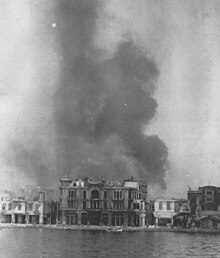 Photo en noir et blanc d'un grand bâtiment face à une rivière en ruine et enfumé.