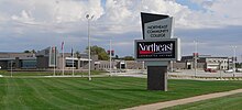 "Northeast Community College" sign on lawn in foreground; low wide-spreading building of fairly recent design behind it