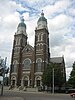 A tall brick church with twin clock towers, topped with domes