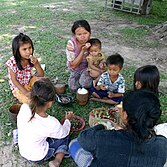 Dos mujeres del sudeste asiático y cinco niños sentados en el césped comiendo arroz y verduras