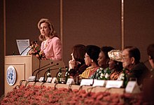 Clinton speaking at a podium with several onlookers