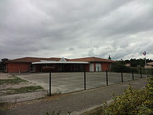 Bâtiment moderne rouge avec auvent et cour en goudron.