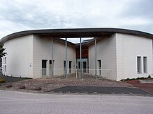 Photographie en couleurs d'un bâtiment moderne en deux parties de part et d'autre d'un porche.