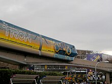 Un monorail que fa un Cicle de Llums pintat que deixa un rastre de color taronja. El segon carretó també porta el títol de Tron Legacy.