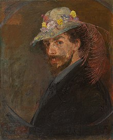 Halbporträt von James Ensor vor bräunlichem Hintergrund. Er trägt einen Vollbart, ein dunkles Gewand und einen hellen Schlapphut, der mit bunten Blumen und einer rosa Feder geschmückt ist.