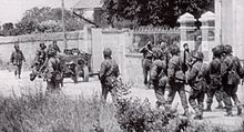 Troupes britanniques de commandos (bérets) et du neuvième bataillon parachutiste (casques et blousons Denison), opérant dans Amfreville en juin 1944.