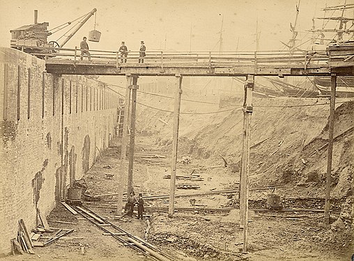 Enlargement (top-hatted directors posing, early 1867). Note sailing ships — held back by temporary earth dam.