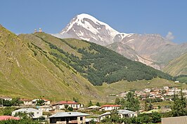 De Kazbek, het dorp Gergeti en boven het dorp de Drievuldigheidskerk van Gergeti