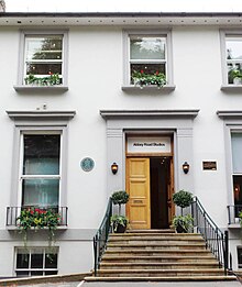 A white, two-story townhouse building with a flight of steps leading to a doorway, above which a sign says Abbey Road Studios.