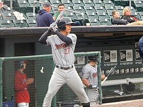 A baseball player in a gray uniform with a navy blue helmet holding a baseball bat in his batting stance