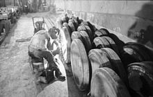 Photographie en noir et blanc montrant un homme ajustant des roues dans un atelier.