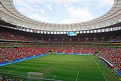 Interior de um estádio, com as arquibancadas e campo levemente cheios