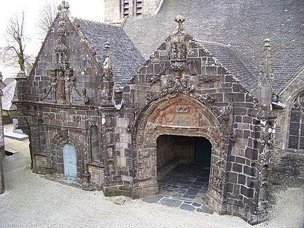 View of the south porch. We see the porch to the right and the two kneeling angels at the top with the two " floating" angels beneath. Above the porch entrance is the tympanum with the Virgin Mary lying on a bed with Joseph at the foot of the bed whilst the heads of two cattle peer out above them. To the left is the ossuary