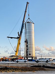 Zdjęcie rakiety przypominającej metalowy silos zbożowy lub duży, kanciasty, niepomalowany termos