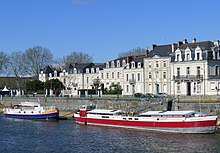 Vue de deux péniches amarrées au bord d'un quai bordé de maisons bourgeoises.