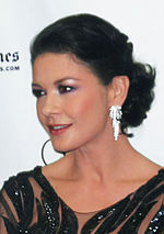 A photo of a black haired woman wearing earrings and a black dress.