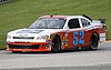 A red and white Chevrolet race car rounds a curve on a racing course.