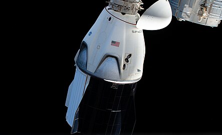 A white spacecraft with a partially black body connects at its head to a off-screen coupler