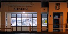 Photographie en couleur de la façade d'un bâtiment blanc, pris de nuit.