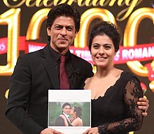 Shahrukh Khan sedang memeluk Kajol sambil memegang sebuah buku meja kopi yang bersampulkan foto seorang laki-laki (Shahrukh) sedang dicium oleh seorang perempuan (Kajol). Pada bagian belakangnya, terdapat tulisan "Celebrating 1000 weeks of timeless romance, Dilwale Dulhania Le Jayenge" atau jika diterjemahkan ke dalam bahasa Indonesia menjadi "Merayakan minggu ke-1000 dari percintaan yang abadi, Dilwale Dulhania Le Jayenge".