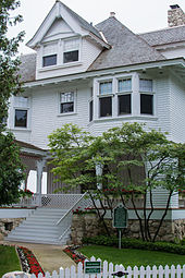 A medium-sized four-story house with wooden siding and a covered porch on the first floor.