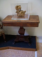 Une couronne brisée sous un cadre de verre, posé sur une table en bois.