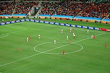 Photo d'un match de football entre une équipe jouant en blanc et l'autre en rouge vu depuis les tribunes