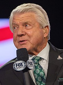 Jimmy Johnson in a suit speaking into a Fox microphone.