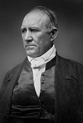 Black-and-white photograph showing a balding man from the chest up. He is looking to the side, with a pensive expression.