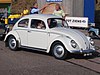 1961 Volkswagen Type 1 "Beetle" with occupants and passersby standing near it.