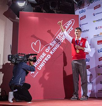 Photo de Steve Guerdat célébrant sa médaille d'or, qu'il a autour du cou, sur la scène de la Maison de la Suisse