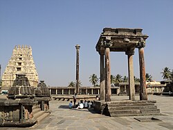 A street in Belur town, Karnataka, India leading to front entrance of the famous Chennakesava temple. The street is lined with shops and houses. A few vehicles are parked on both sides of the street. There are some pedestrians.