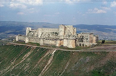 An enormous castle with encircling walls, on a rise in barren country with distant mountains.