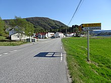 Foto einer Straße die an einigen Häusern vorbeiführt. Im Hintergrund eine Erhebung