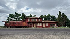 An isolated two-story rail station with a Santa Fe caboose to the left