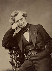 photograph of elderly man, sitting at a table, resting his head on his right hand