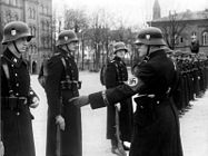 Unge kadetter i nazilederen Adolf Hitlers vaktstyrke LSSAH i Berlin høsten 1938. Soldatene er uniformert i tunge stålhjelmer og svarte frakker merket med doble siegruner som tegn på Schutzstaffel (SS). Hjelmens venstre side og armbindet er dekorert med hakekors, nazistenes hovedsymbol. Foto: Deutsches Bundesarchiv