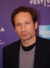 A man with dark brown hair is smirking and looking near the camera.