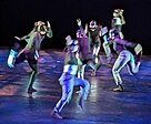 Group of dancers in black and metallic colors in exaggerated running poses pointing in various directions