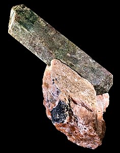 Fluorapatite: Long, prismatic crystal, dull in lustre, protruding, at an angle, from matrix of aggregate-like rock