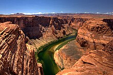 View of a narrow green river flowing between high, reddish-brown cliffs