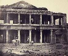 A photograph of the ruins of a palace with human skeletal remains in the foreground