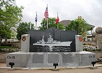 Small stone memorial in the shape of a ship depicting a ship with flags in the background