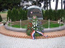 Un momument commémoratif, avec des inscriptions en serbo-croate i en allemand à la mémoire de la "tragédie de Bleiburg"; devant le momument, une gerbe de fleurs aux couleurs du drapeau croate.