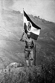 Un Askari brandissant un drapeau impérial allemand en Afrique orientale allemande (vers 1910).